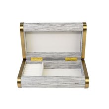 Front view of open Orion box with textured grey and white PVC, gold hardware and cream suede-lined inner compartments for jewelry