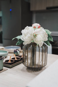 Styled photo of clear Abbott vase with white flowers and green leaves on a light brown dining table