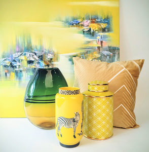 Village at Sunrise Painting serves as a vivid backdrop for yellow and gold-themed home decor accessories like vases, jar and cushion.
