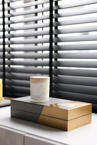 Chelsea box with white candle on a light grey side console in front of black window blinds