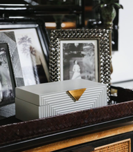 Grey Hamilton box in front of two silver photoframes on a dark brown woven tray