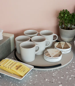 Styled photo of two sets of Aiden coasters placed next to some white mugs on a round grey and black leather tray